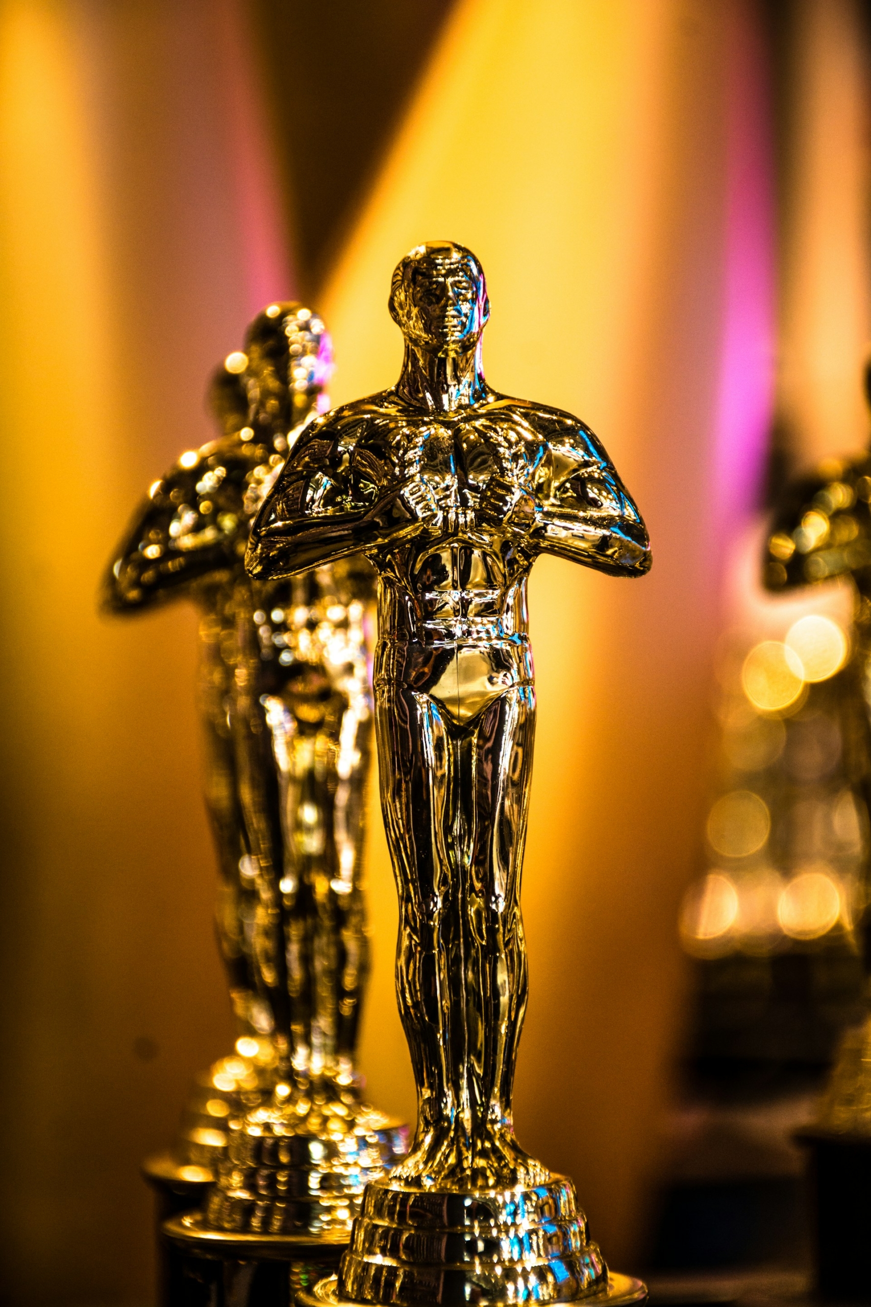 Two oscars awards displayed in front of a bright golden background