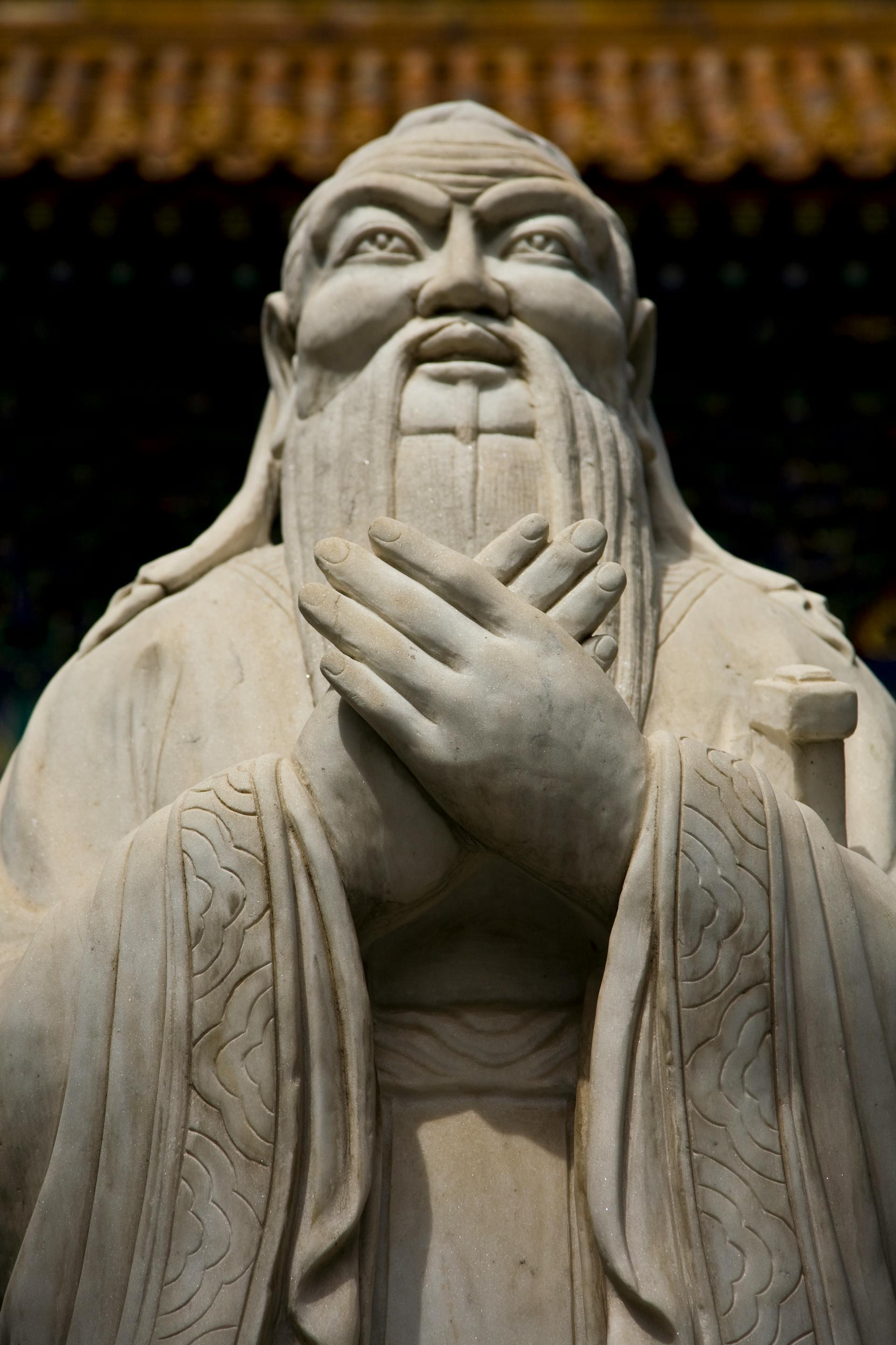 A close-up of a marble statue depicting a figure with intricate robes and hands clasped in front, showcasing fine details and craftsmanship.