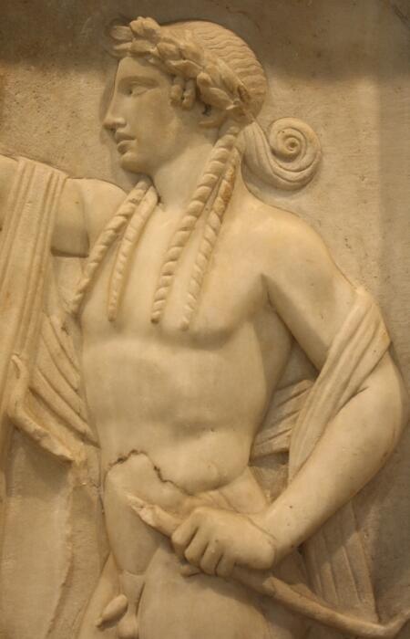 Marble relief of a muscular figure in ancient attire, holding a staff. The figure wears a laurel wreath, conveying a sense of dignity and strength.