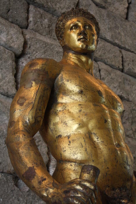 A golden metal sculpture representing Hercules, the Greek god associated with strength.