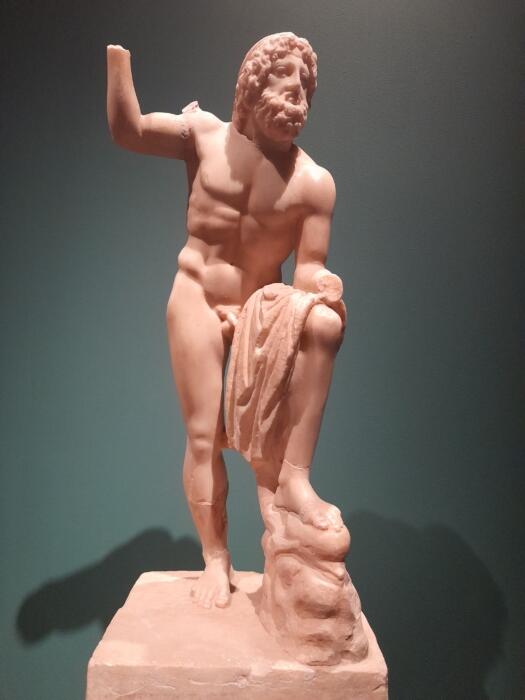 Marble sculpture of a bearded man with wavy hair, standing nude on a pedestal, draped cloth in one hand, conveys strength and classical elegance.