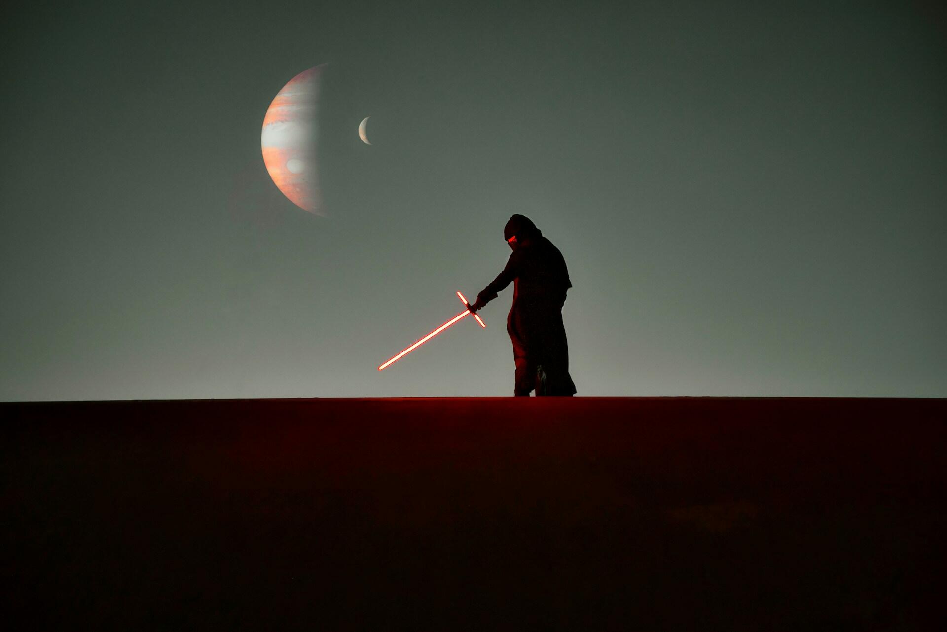 A man stands on a hill, wielding a red lightsaber, evoking a scene from Star Wars.